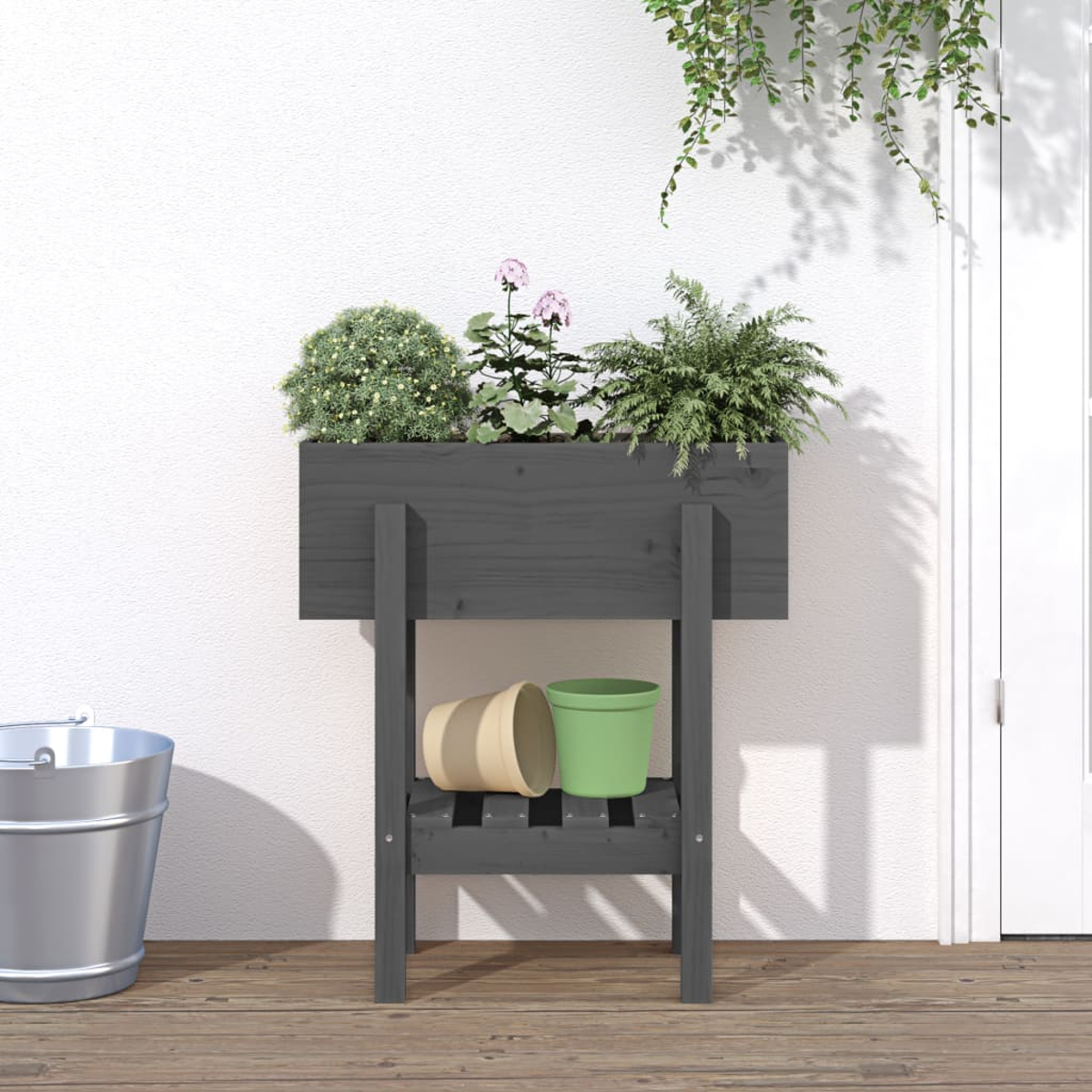 Ein grauer Blumenkasten auf Beinen mit Pflanzen, Eimern und Töpfen.