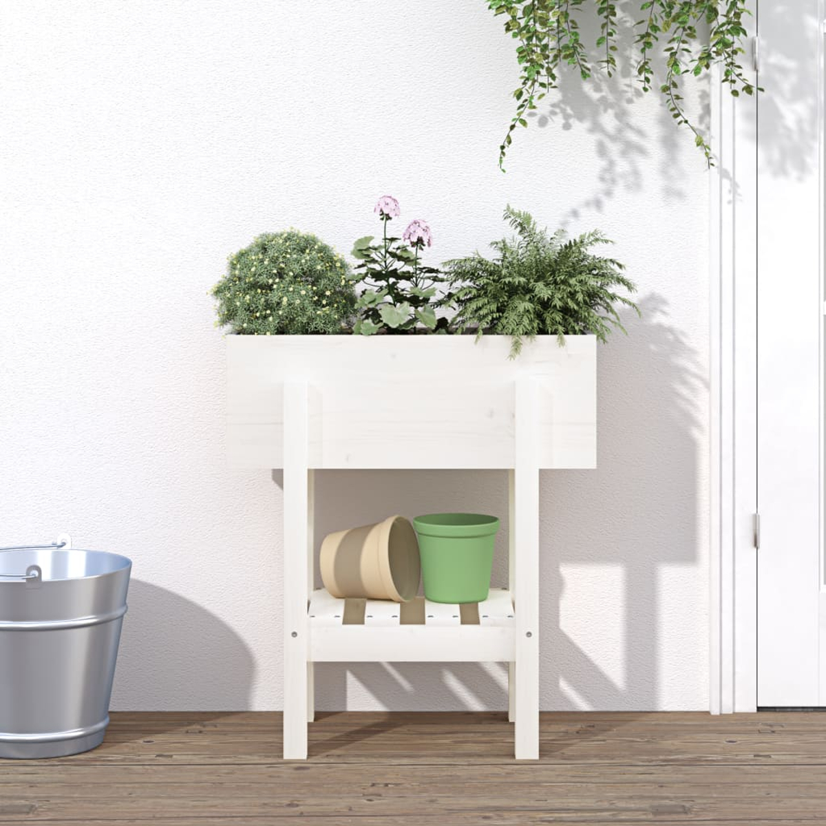 Ein weißer Blumenkasten mit Pflanzen steht auf einer Holzterrasse neben einem Metalleimer.
