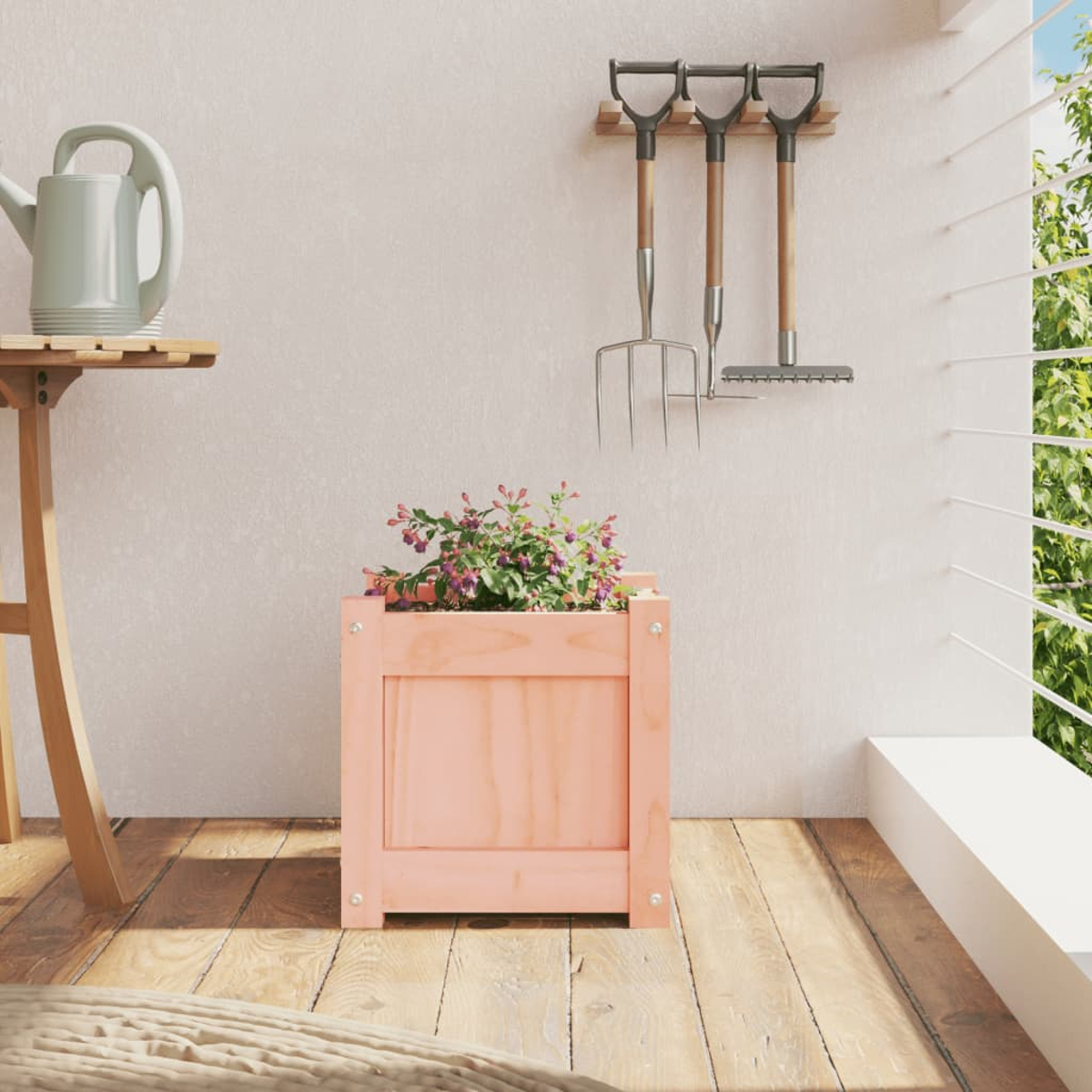 Ein rosa Pflanzer mit Blumen steht auf einem Holzbalkon neben Gartengeräten.