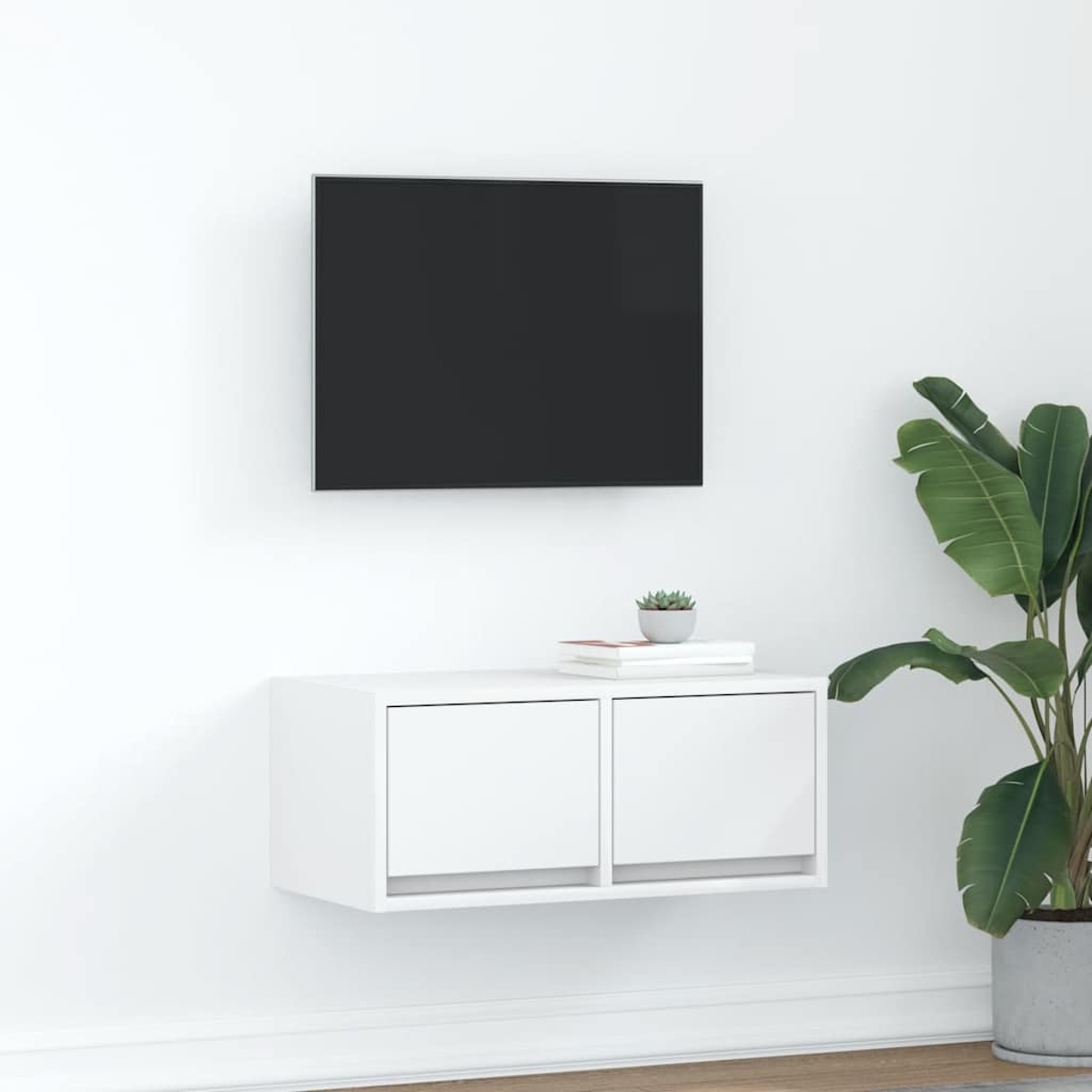 Ein moderner weißer schwebender TV-Ständer mit zwei Schubladen, einem darüber montierten TV und einer Pflanze.