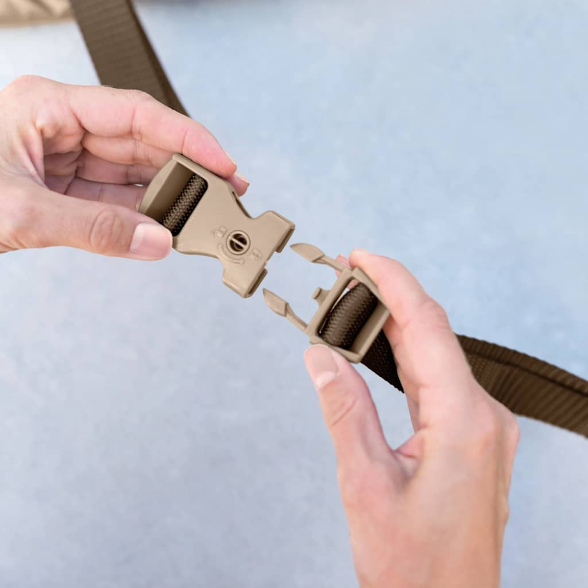 Dwie ręce zapinają brązowy pasek plastikową klamrą na jasnoniebieskim tle.