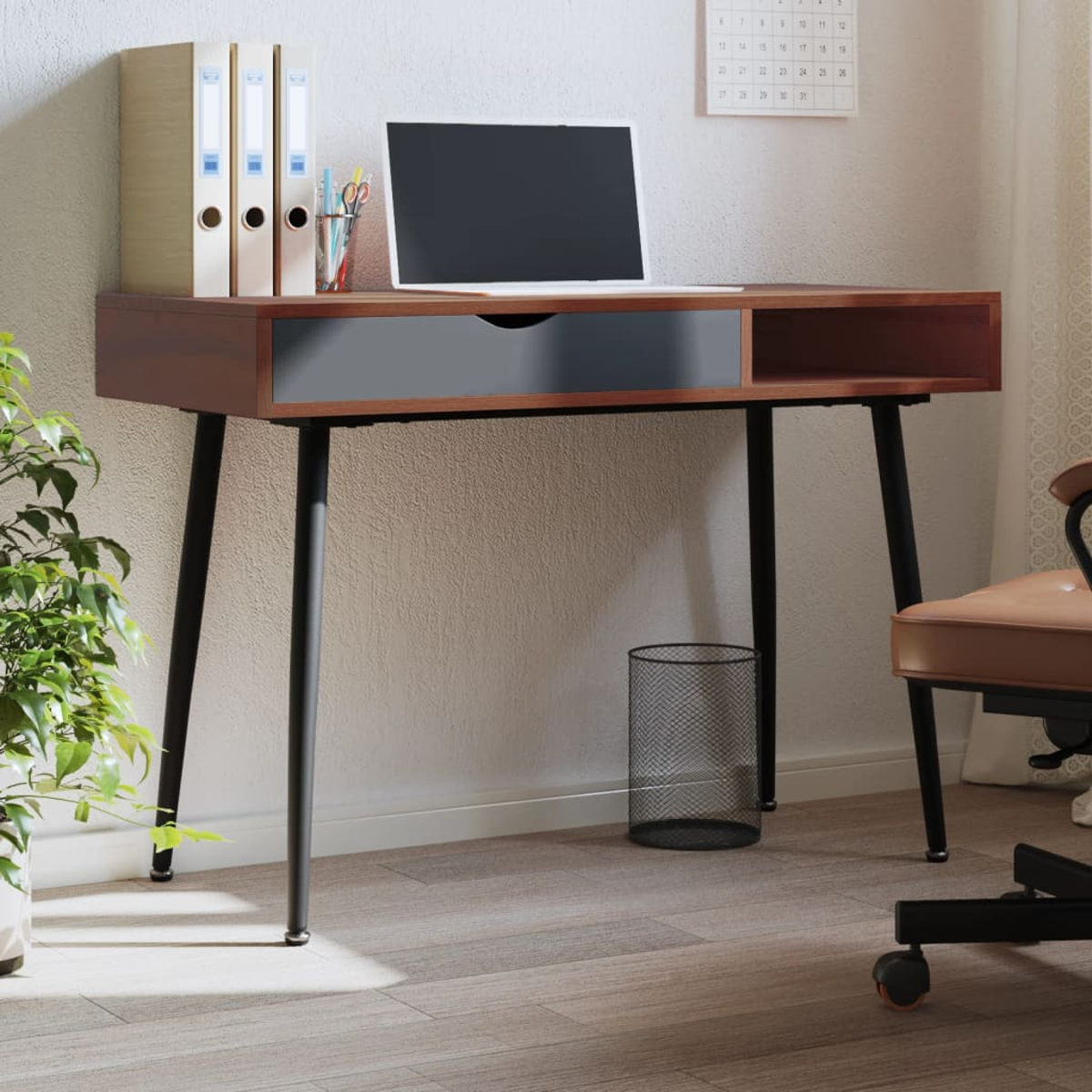 Ein brauner Schreibtisch mit schwarzen Beinen, Laptop, Ordnern und einem Mülleimer.