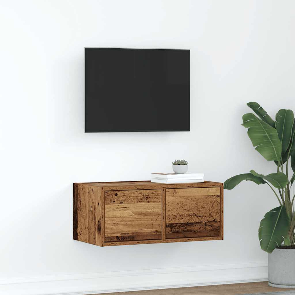 Un televisor montado en la pared sobre un mueble rústico de madera con libros y una planta.