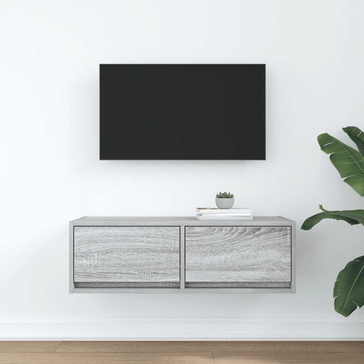 Ein moderner schwebender TV-Ständer mit zwei Schubladen, einem schwarzen Fernseher darüber und einer Pflanze.
