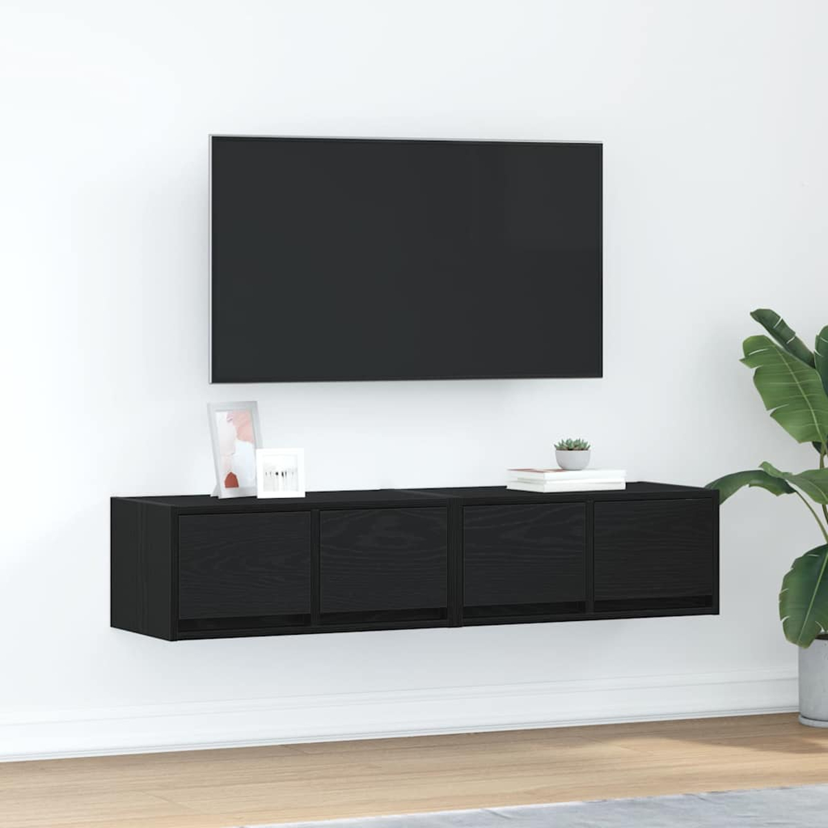 Ein schwarzer Wand-TV-Schrank trägt Bilderrahmen, Bücher und eine Pflanze. Oben hängt ein Fernseher.