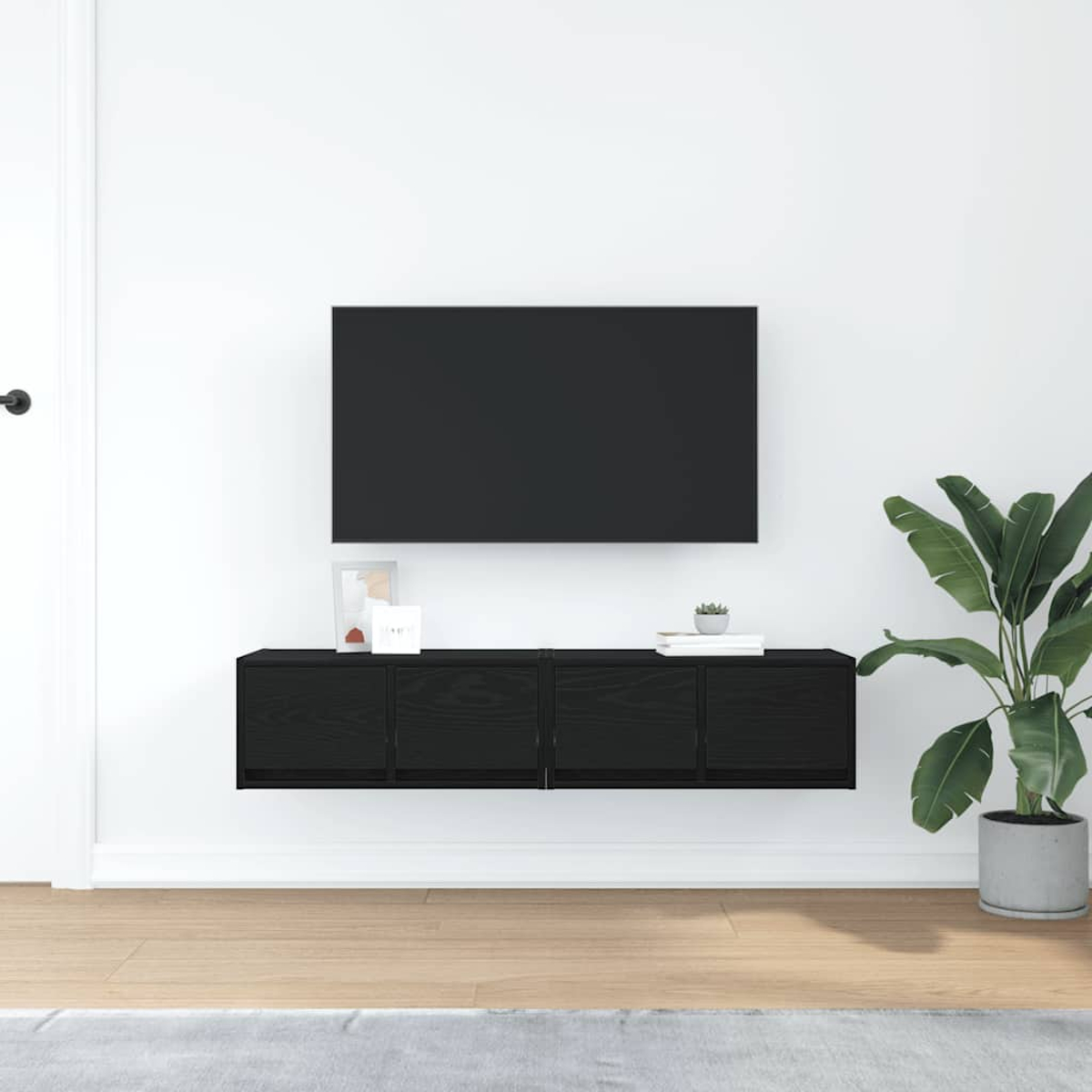 Ein schwarzer Wand-TV und Schrank in einem Raum mit Pflanze.