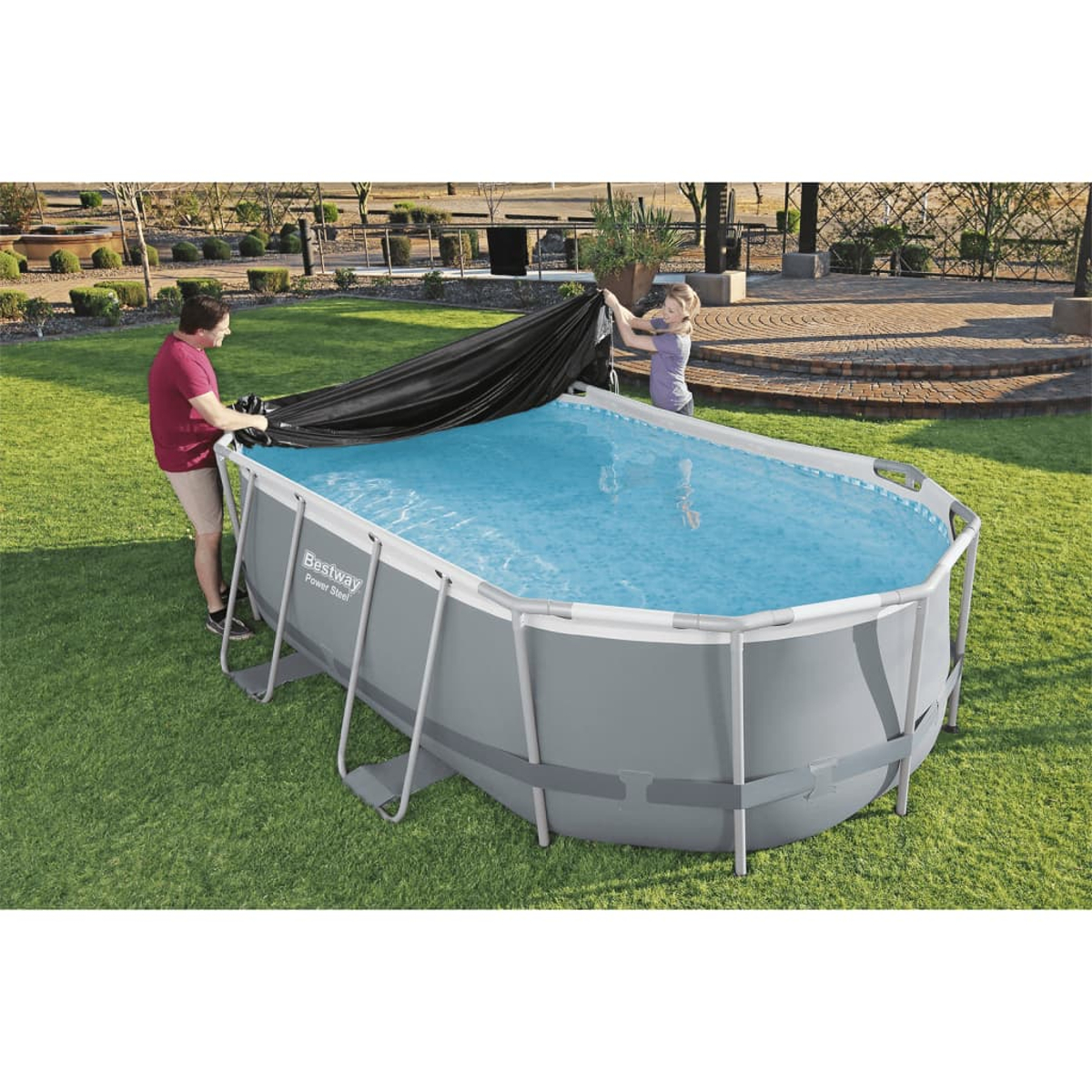 Mann und Frau bedecken einen ovalen Pool an einem sonnigen Tag mit schwarzer Abdeckung.