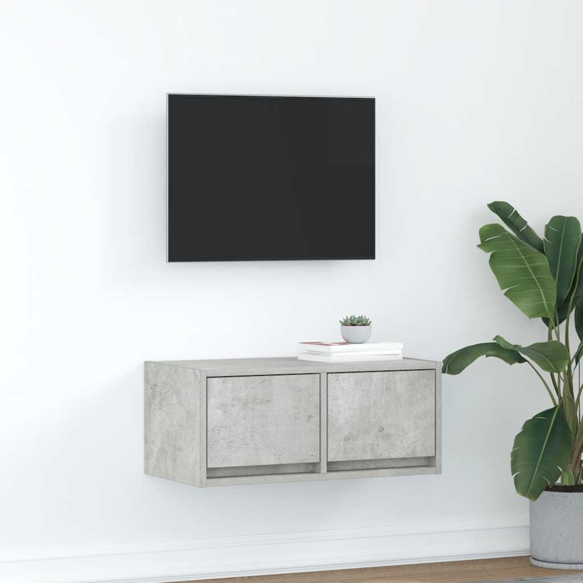 Ein wandmontierter grauer Schrank mit zwei Türen unter einem schwarzen Fernseher. Rechts steht eine Pflanze.