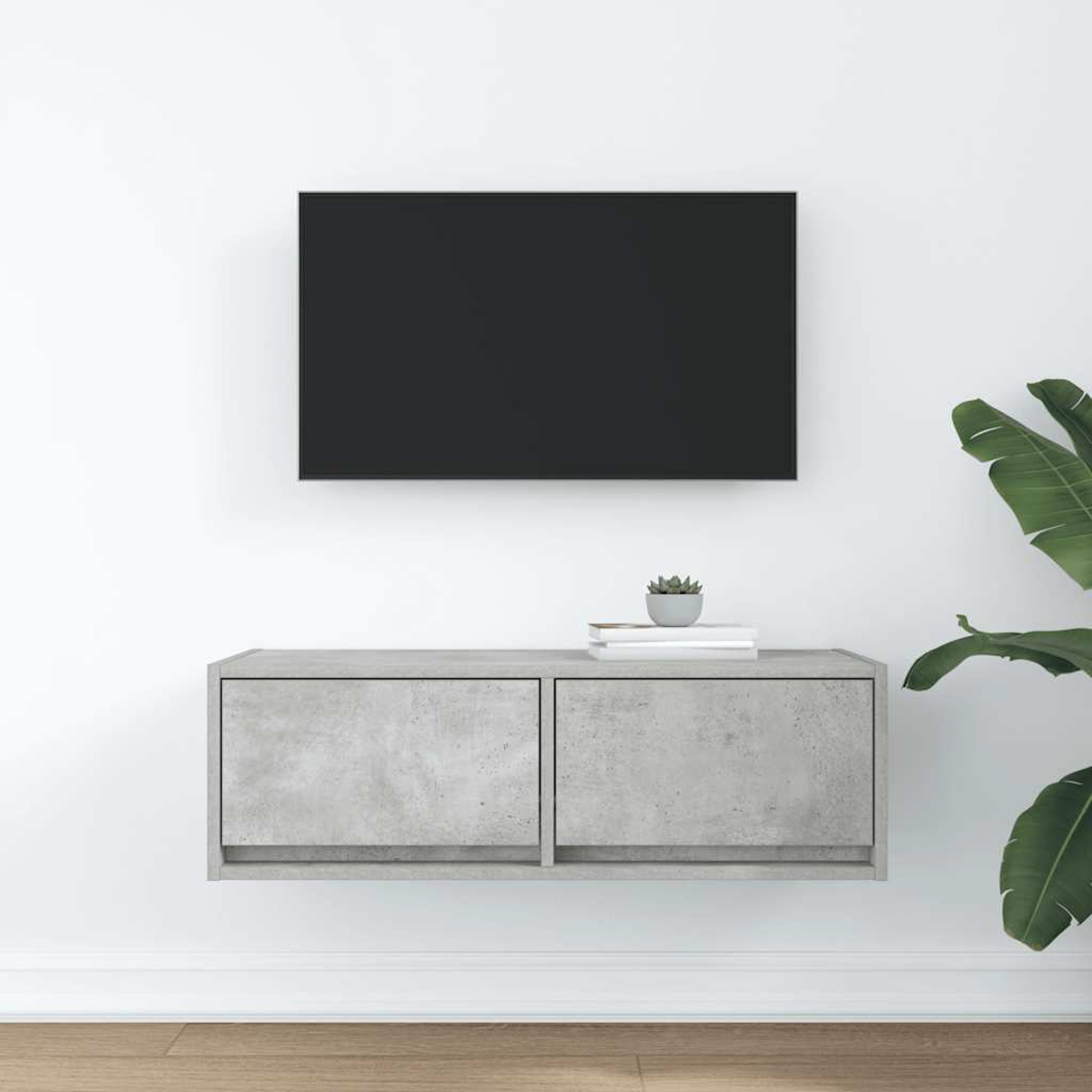 Ein an der Wand montierter Fernseher über einem grauen Schrank mit Büchern und einer Pflanze.