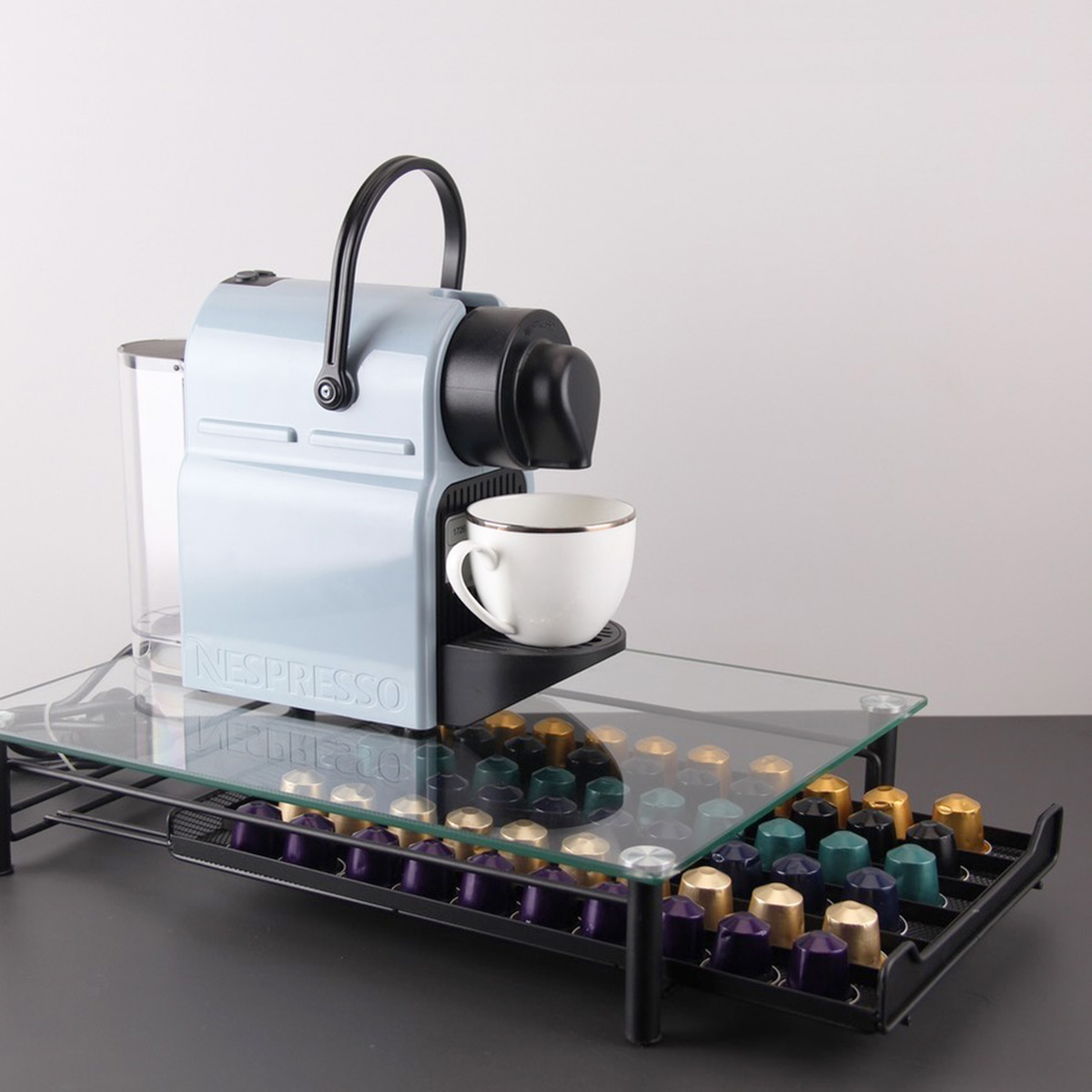 Una cafetera Nespresso azul claro con una taza blanca y muchas cápsulas de café.
