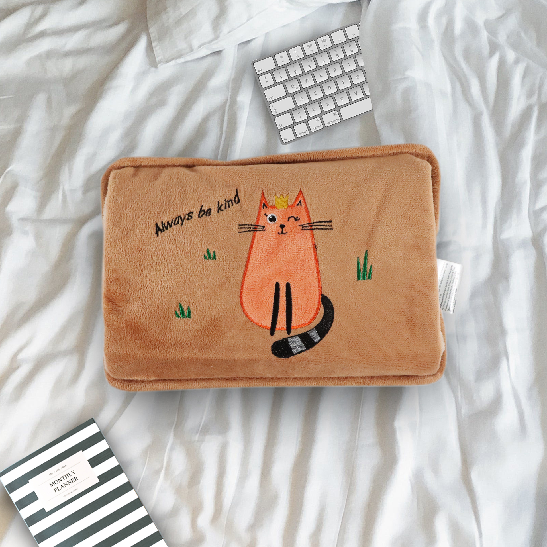 Una almohada marrón con un gato y texto, sobre una cama blanca con un teclado.