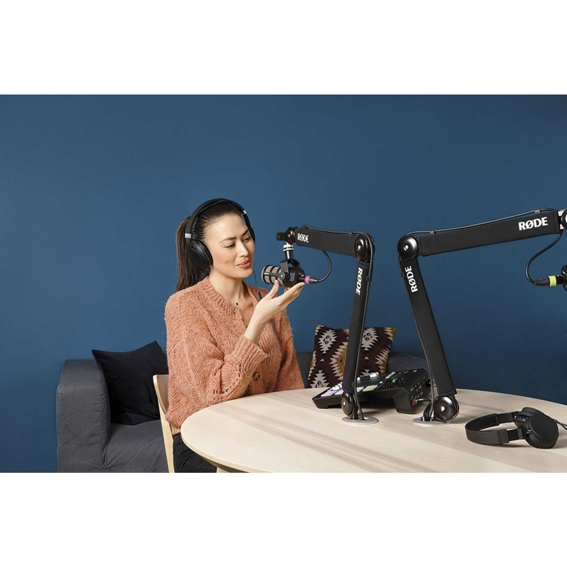 Kobieta w słuchawkach siedzi przy stole z mikrofonami i sprzętem audio.