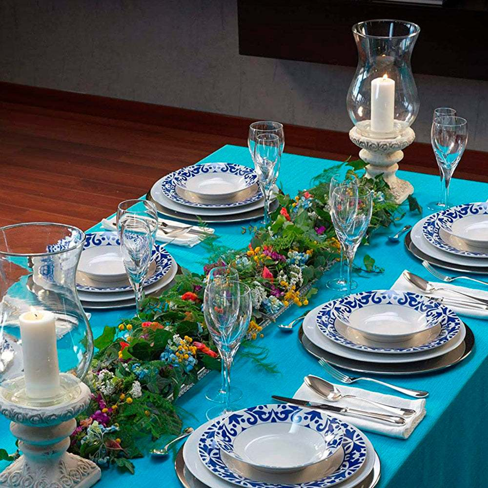 Un montaje de mesa formal con platos azules y blancos, copas de cristal y un centro floral.