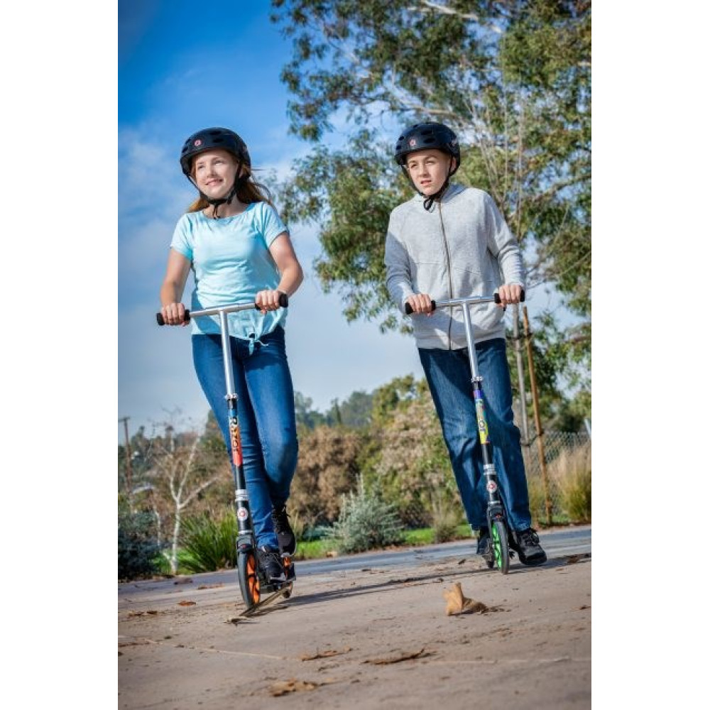 Two children wearing helmets ride scooters on an outdoor path.