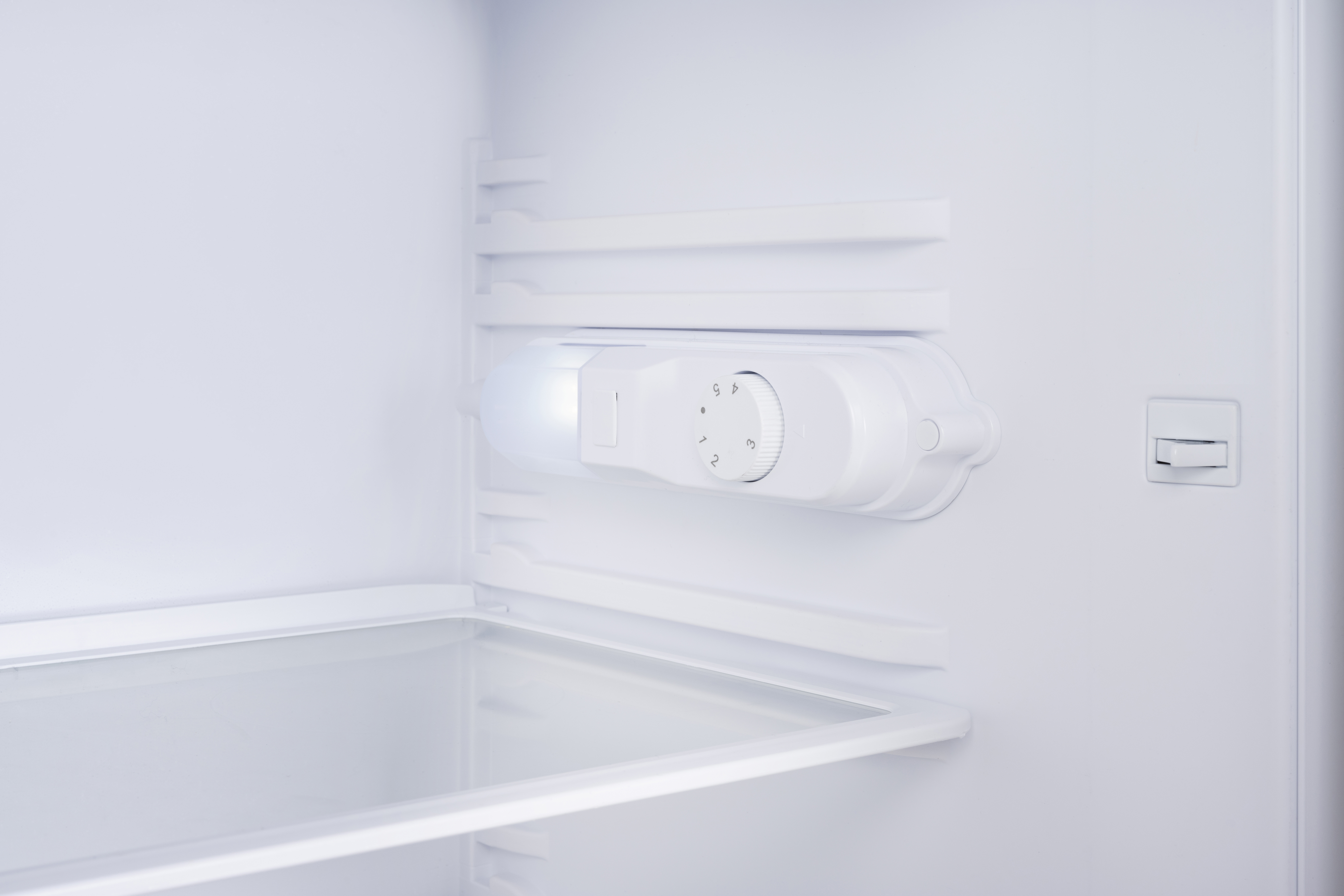 Een lege koelkast met een thermostaatknop en een lamp.