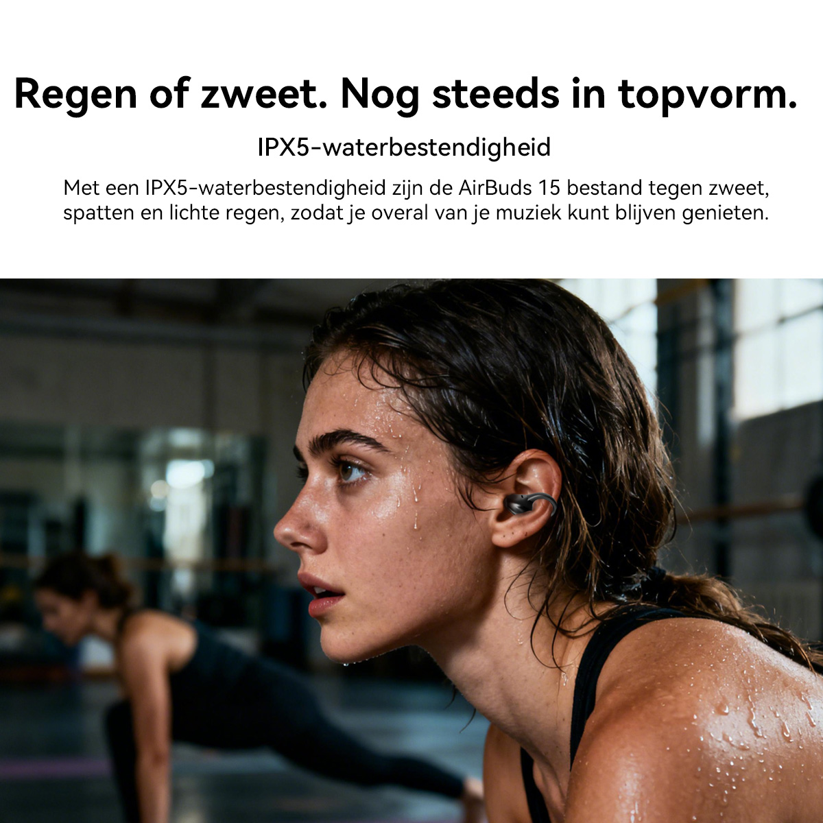Een bezwete vrouw met oordopjes in een sportschool, een ander traint op de achtergrond.