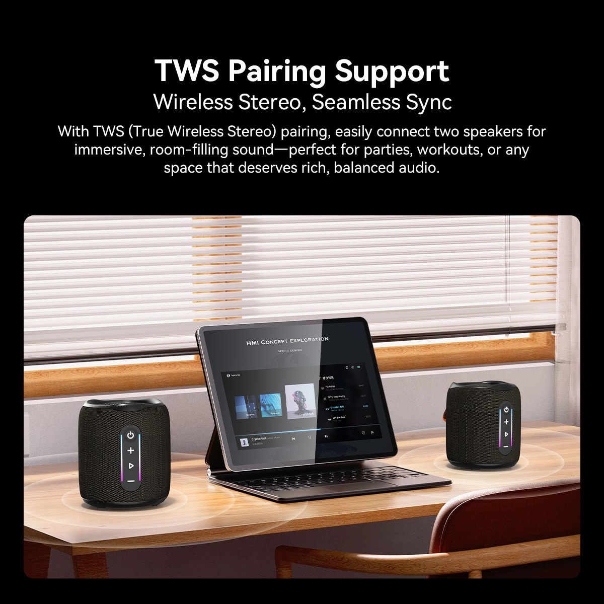 Two black speakers on a desk next to a tablet displaying music.