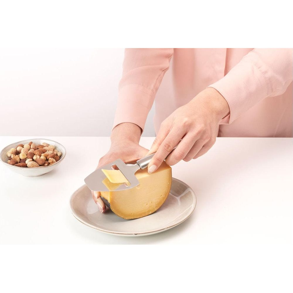 Una persona affetta formaggio con un'affettatrice per formaggio. Una ciotola di noci è vicina.