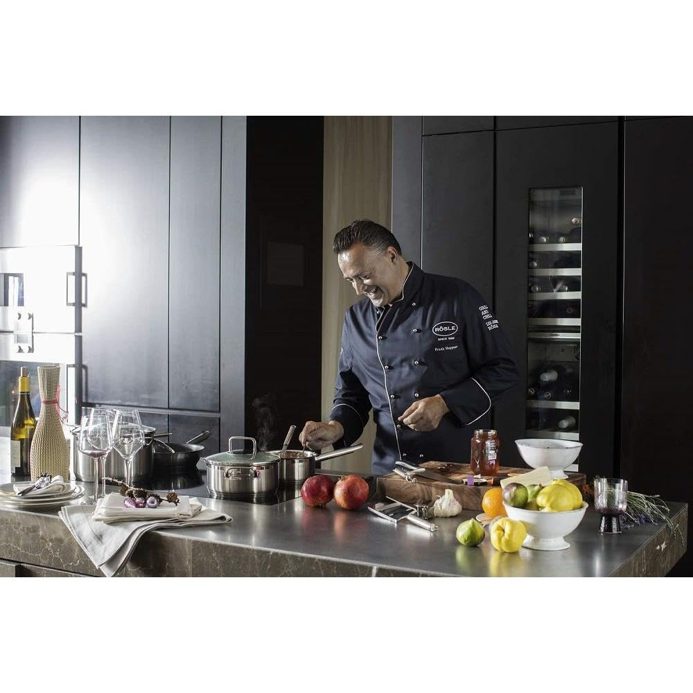 Uno chef in divisa blu cucina in una cucina moderna. Frutta e vino sul bancone.