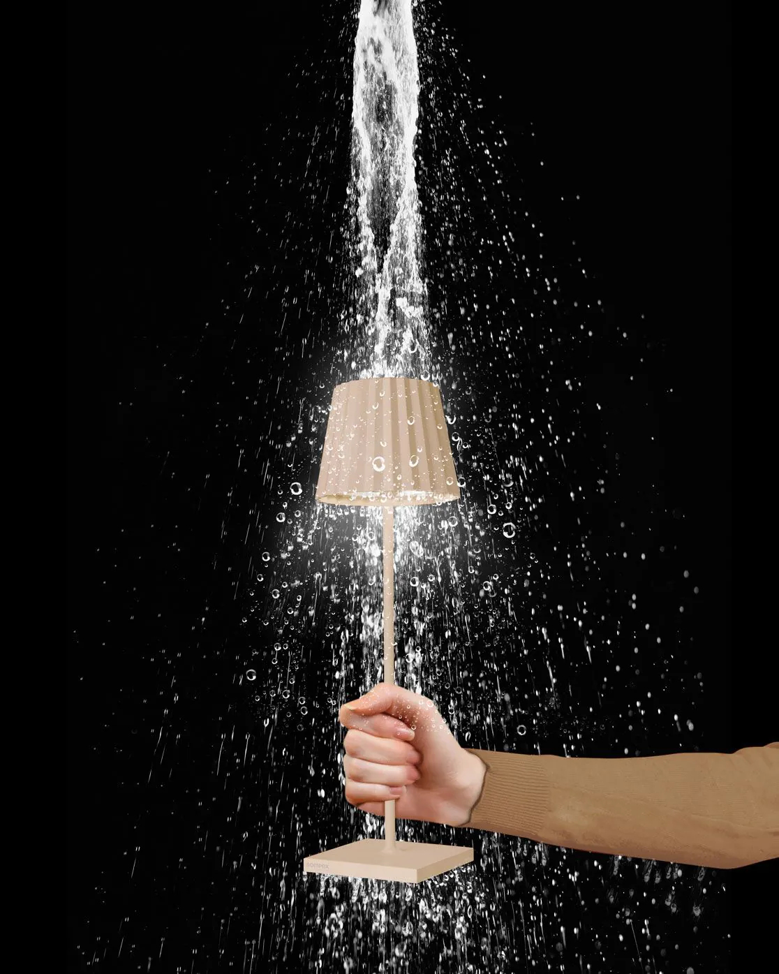 Eine Hand hält eine Lampe, während Wasser darauf spritzt. Schwarzer Hintergrund.