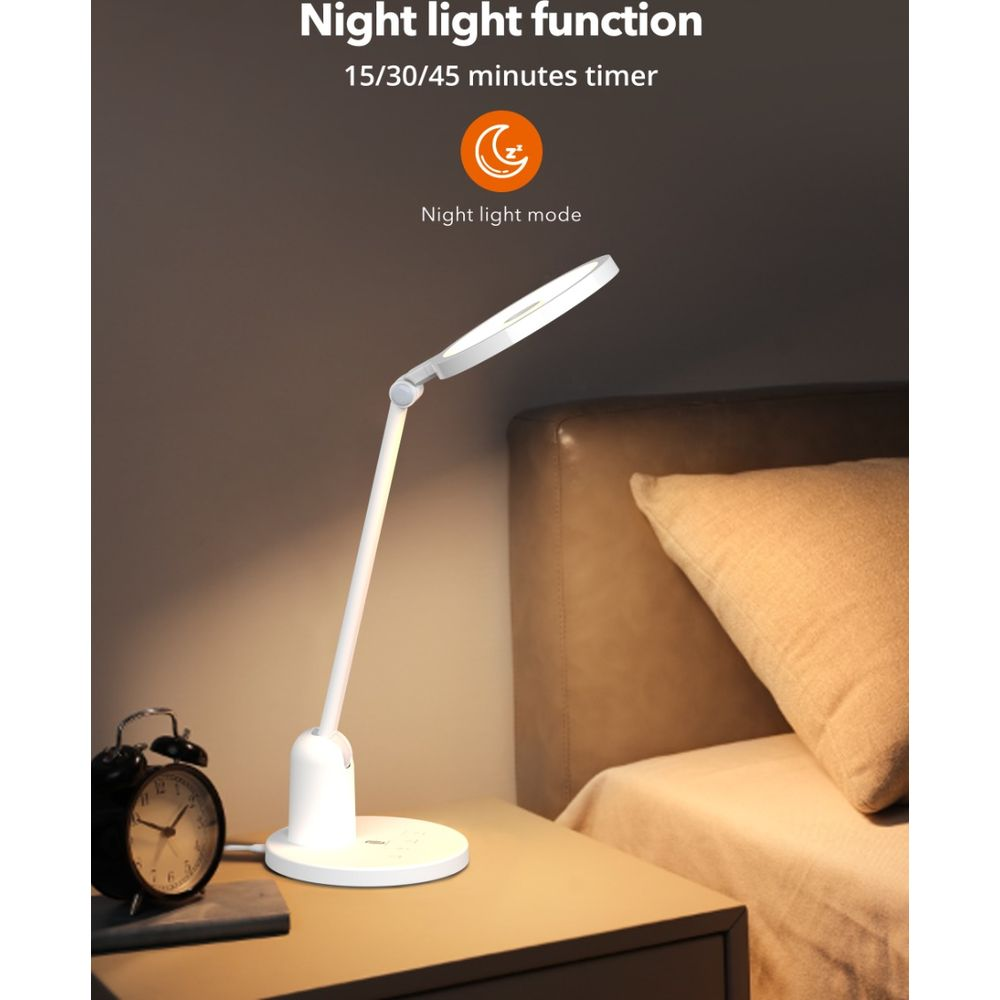 Eine weiße, verstellbare Schreibtischlampe mit Nachtlichtfunktion steht auf einem Nachttisch neben einem Bett.