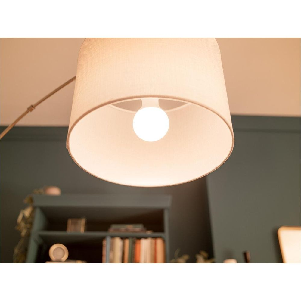 Une ampoule LED blanche allumée à l'intérieur d'un abat-jour beige. Une étagère à livres est visible à l'arrière-plan.