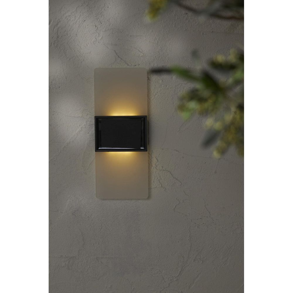 Eine rechteckige Wandleuchte mit schwarzem Rahmen und warmem Licht leuchtet.