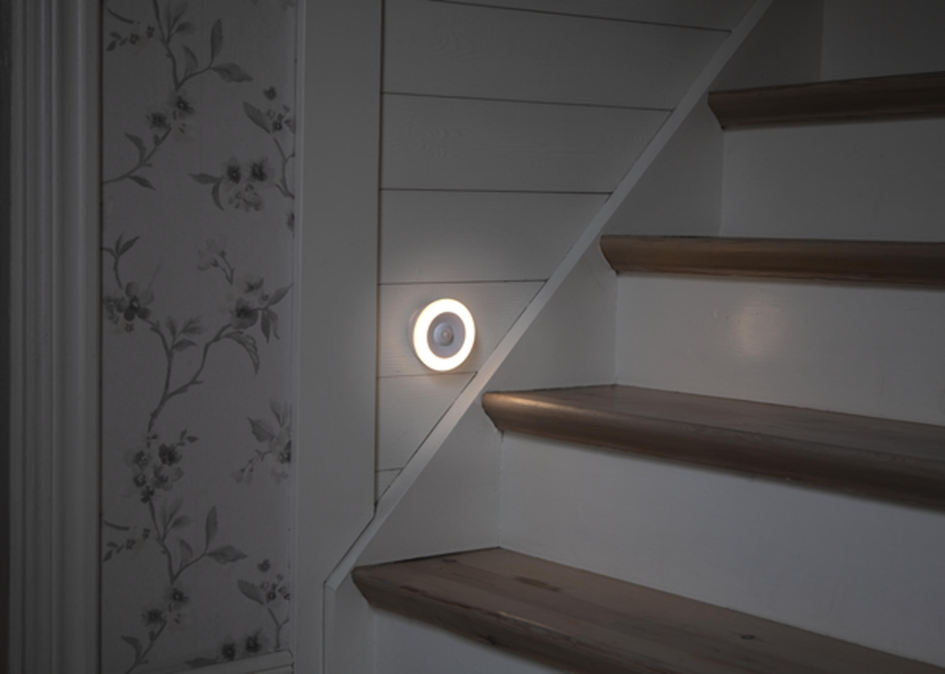Un capteur LED rond avec une lumière blanche éclaire un escalier en bois.