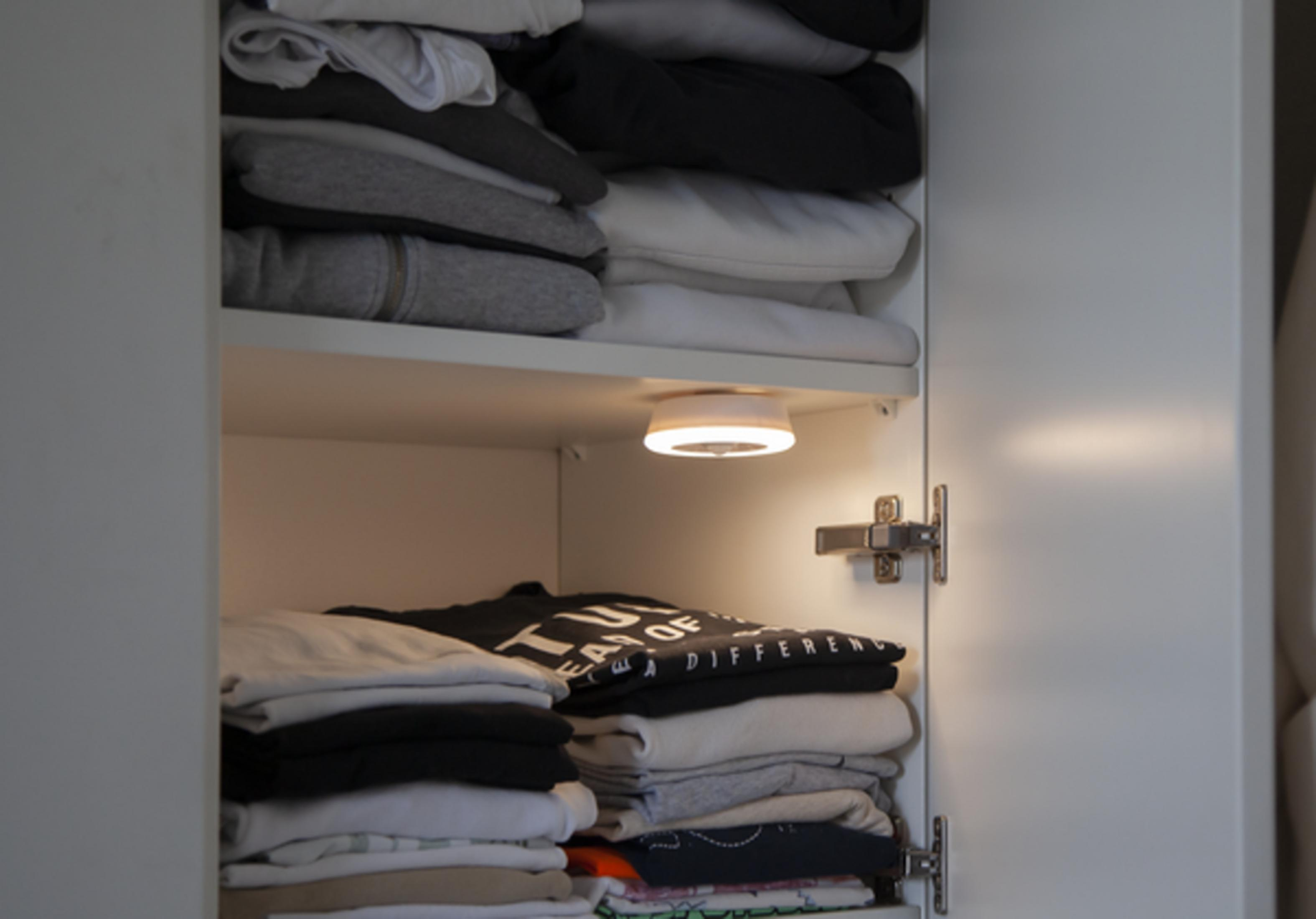 Une armoire blanche ouverte avec des vêtements gris, noirs et blancs empilés proprement.