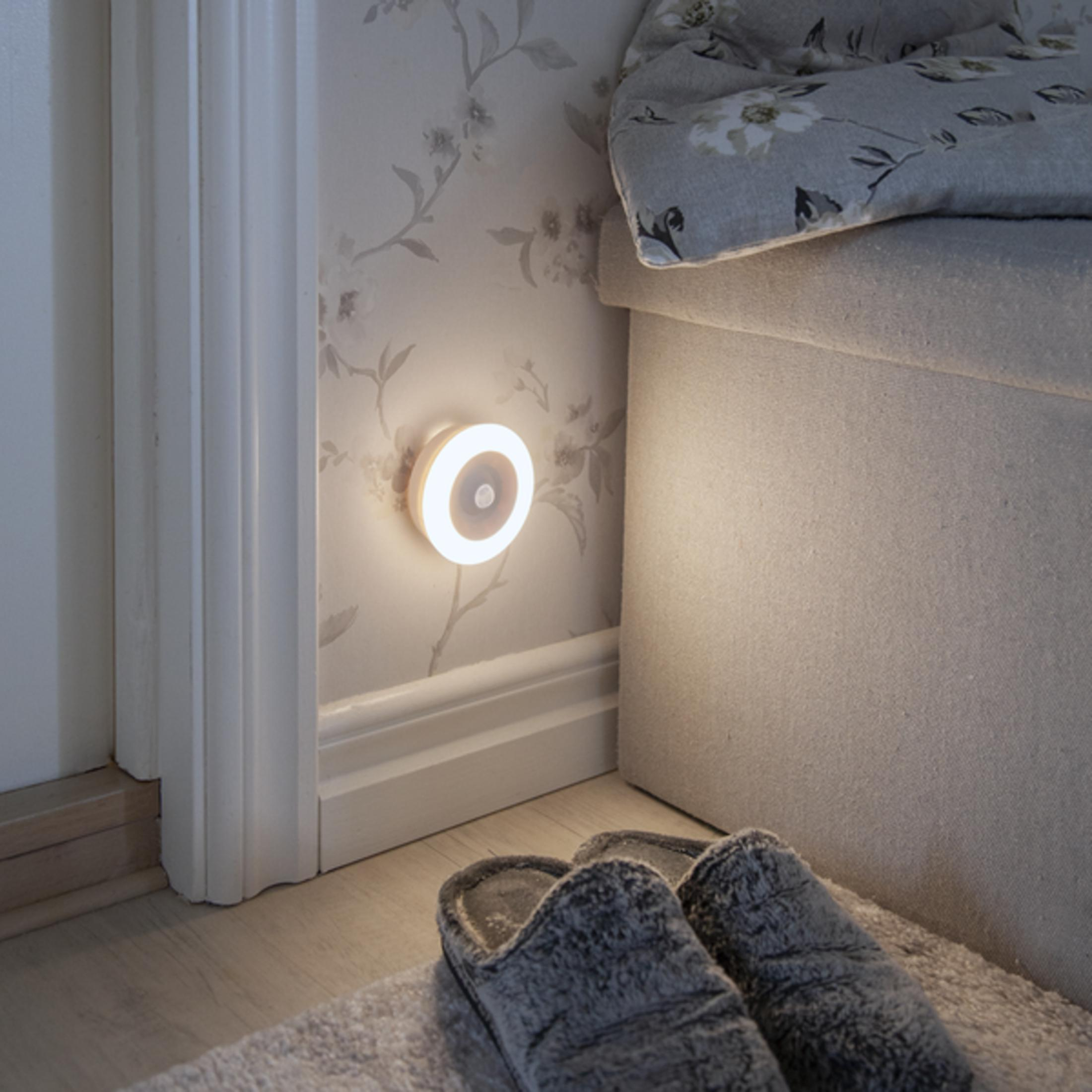 Une veilleuse ronde brille sur un papier peint floral. Des chaussons reposent sur un tapis.