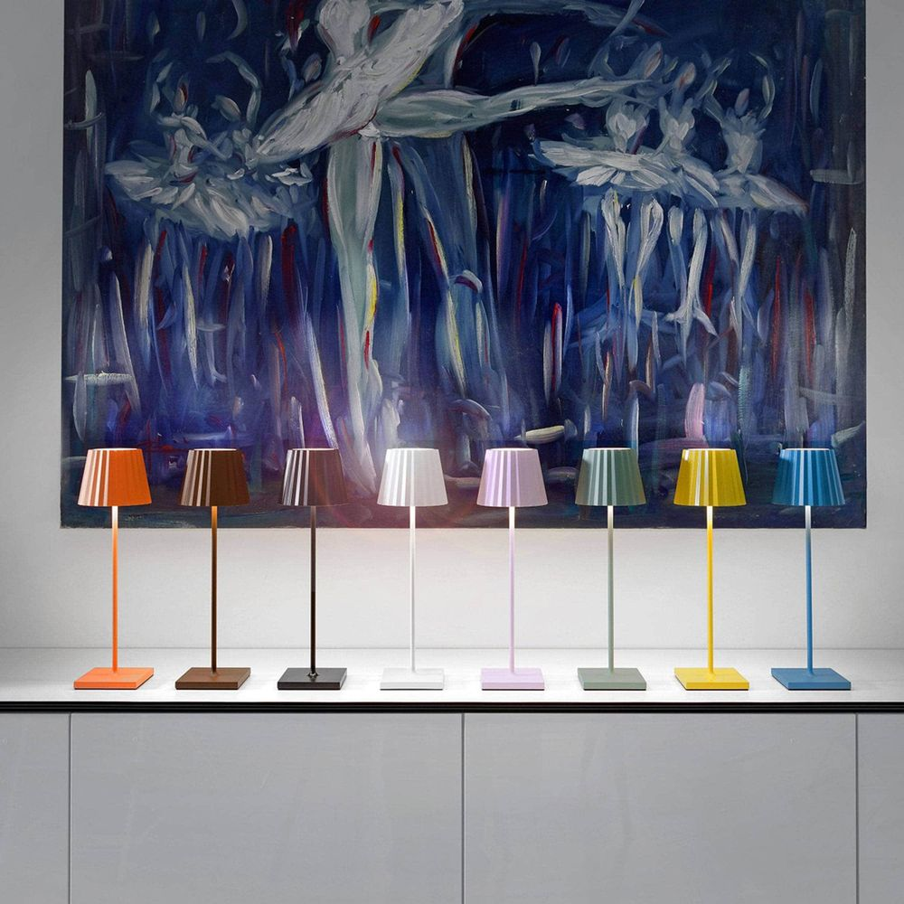 Sette lampade da tavolo colorate davanti a un dipinto di ballerine.