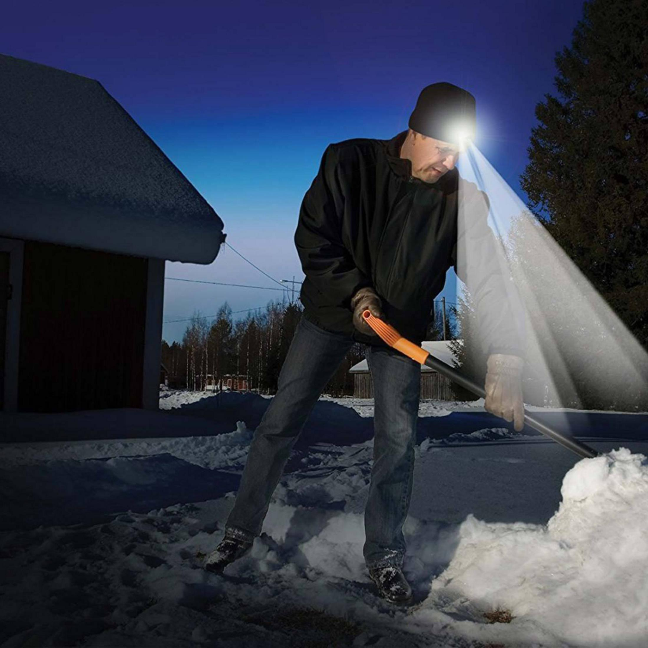 Homme pelletant la neige la nuit avec une lampe frontale.