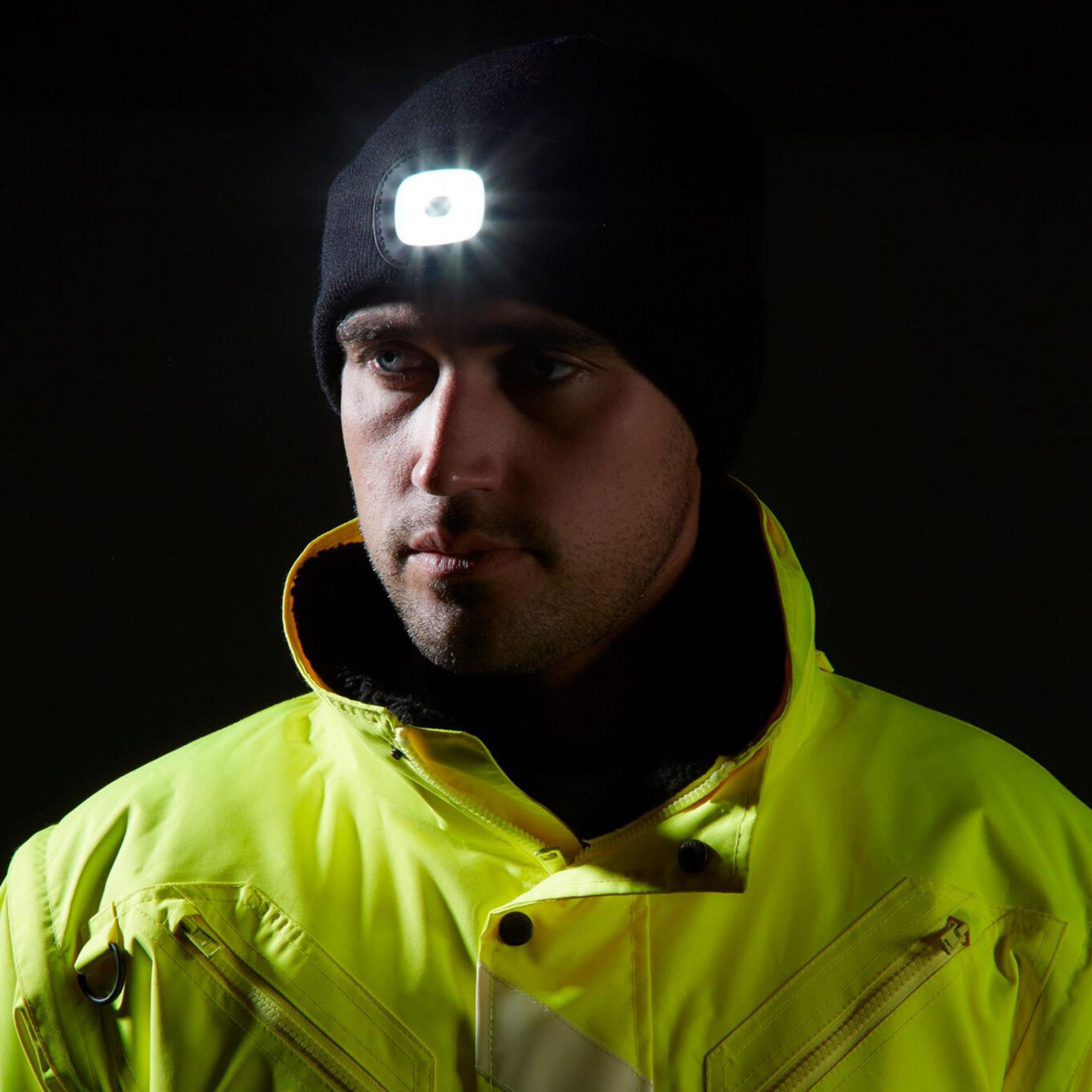 Homme portant un bonnet noir avec lampe frontale et une veste jaune fluo.