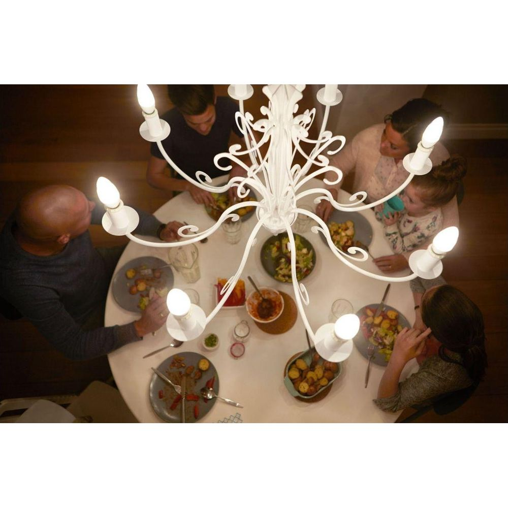 Une famille partage un repas autour d'une table blanche sous un lustre blanc.