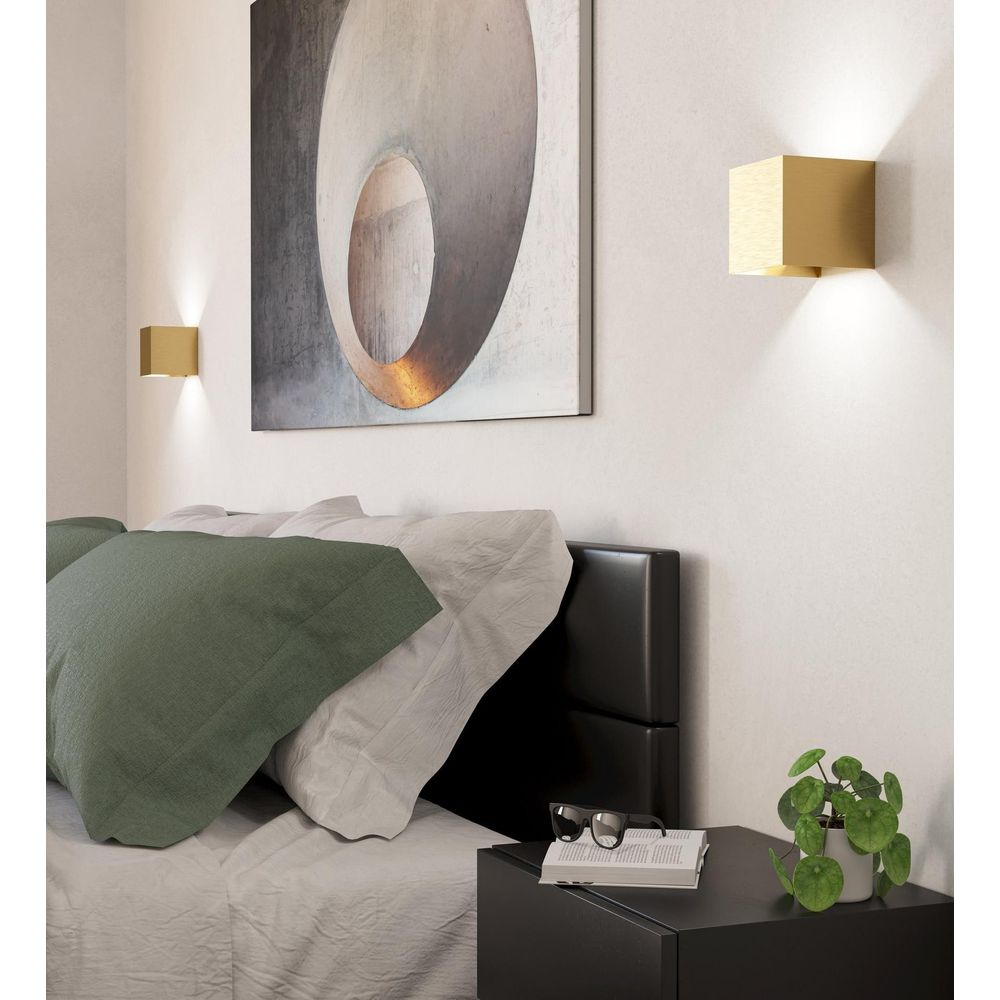 Chambre moderne avec applique cube doré, art abstrait et lit avec oreillers verts et blancs.