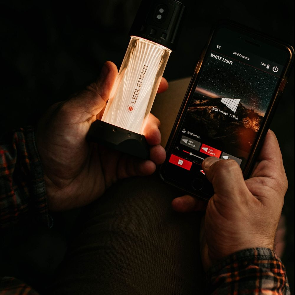 Une main tient une lanterne allumée, l'autre un smartphone avec une application.