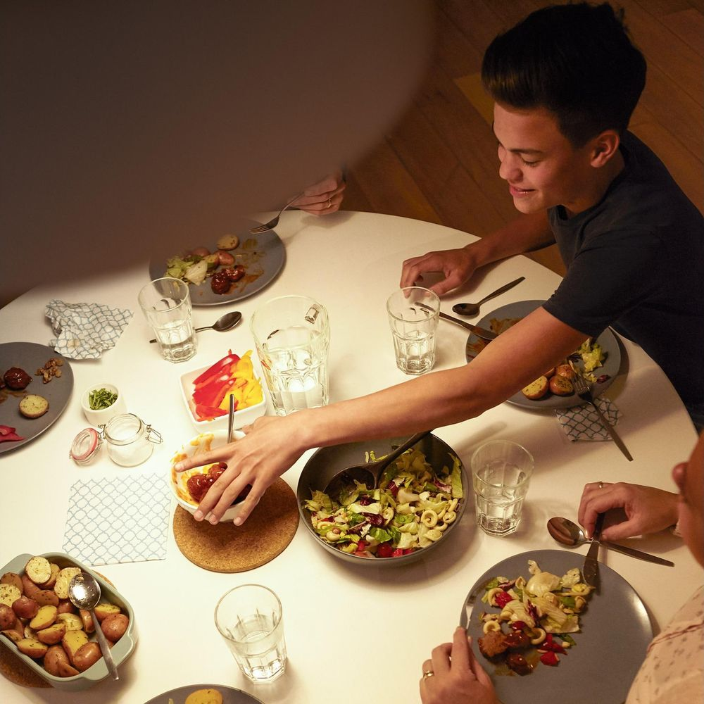 Persone che mangiano a un tavolo rotondo con insalate, patate e piatti di carne.