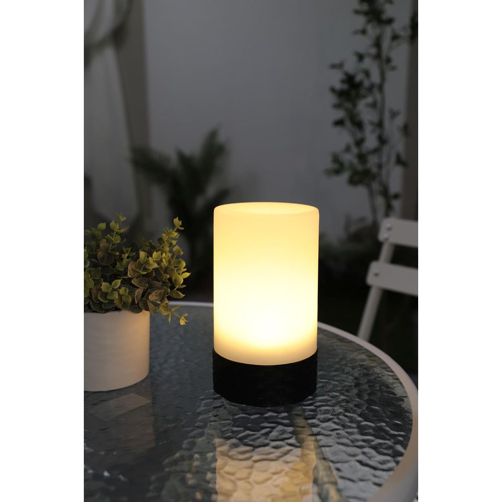Eine beleuchtete Lampe und eine Topfpflanze stehen auf einem Glastisch im Freien.