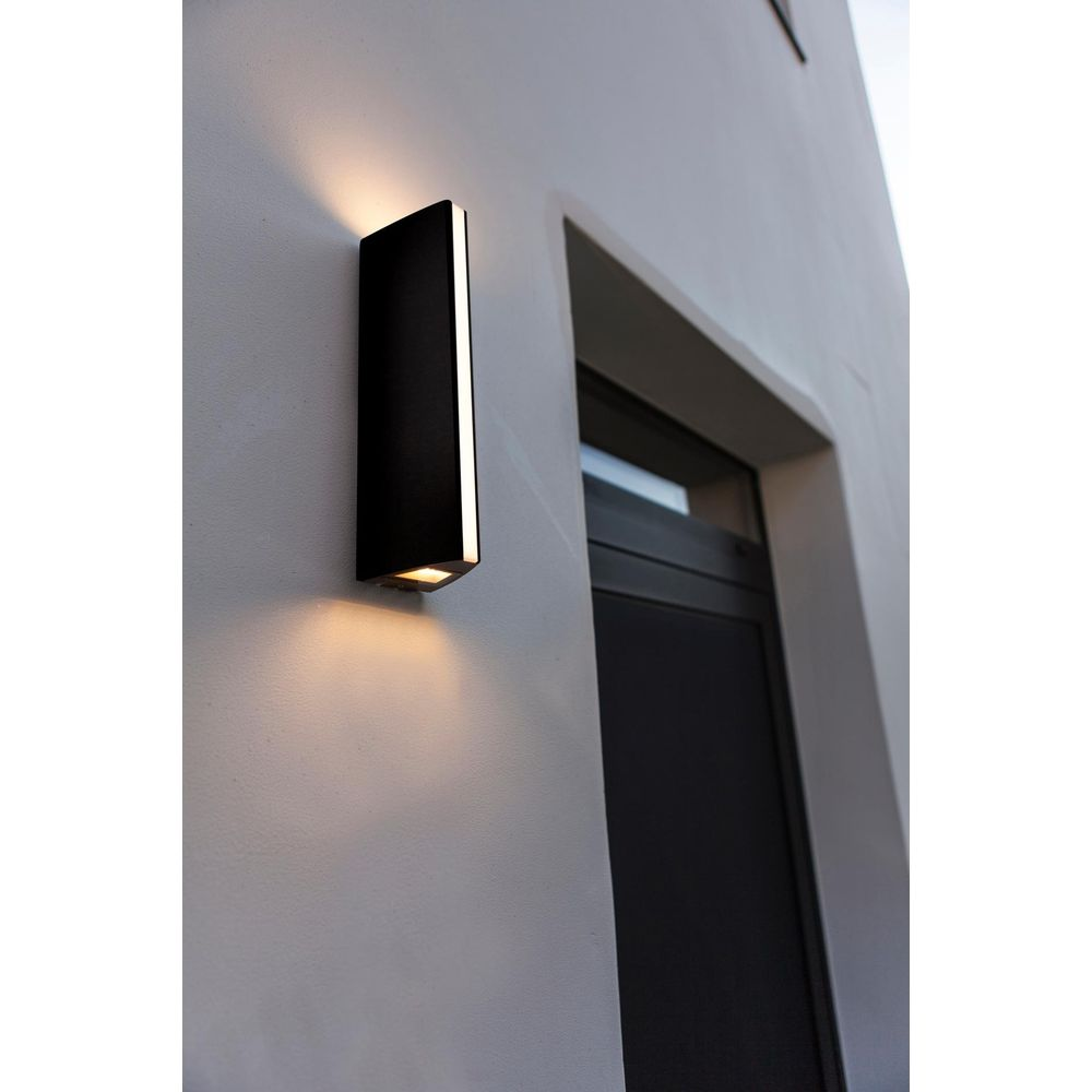 Schwarze Wandleuchte beleuchtet weiße Wand neben dunkler Tür.