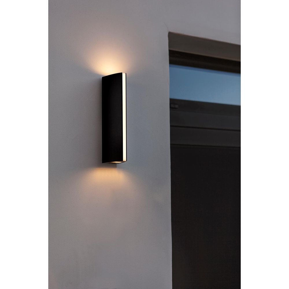 Schwarzer Wandleuchter beleuchtet Wand und Fenster mit warmem Licht.