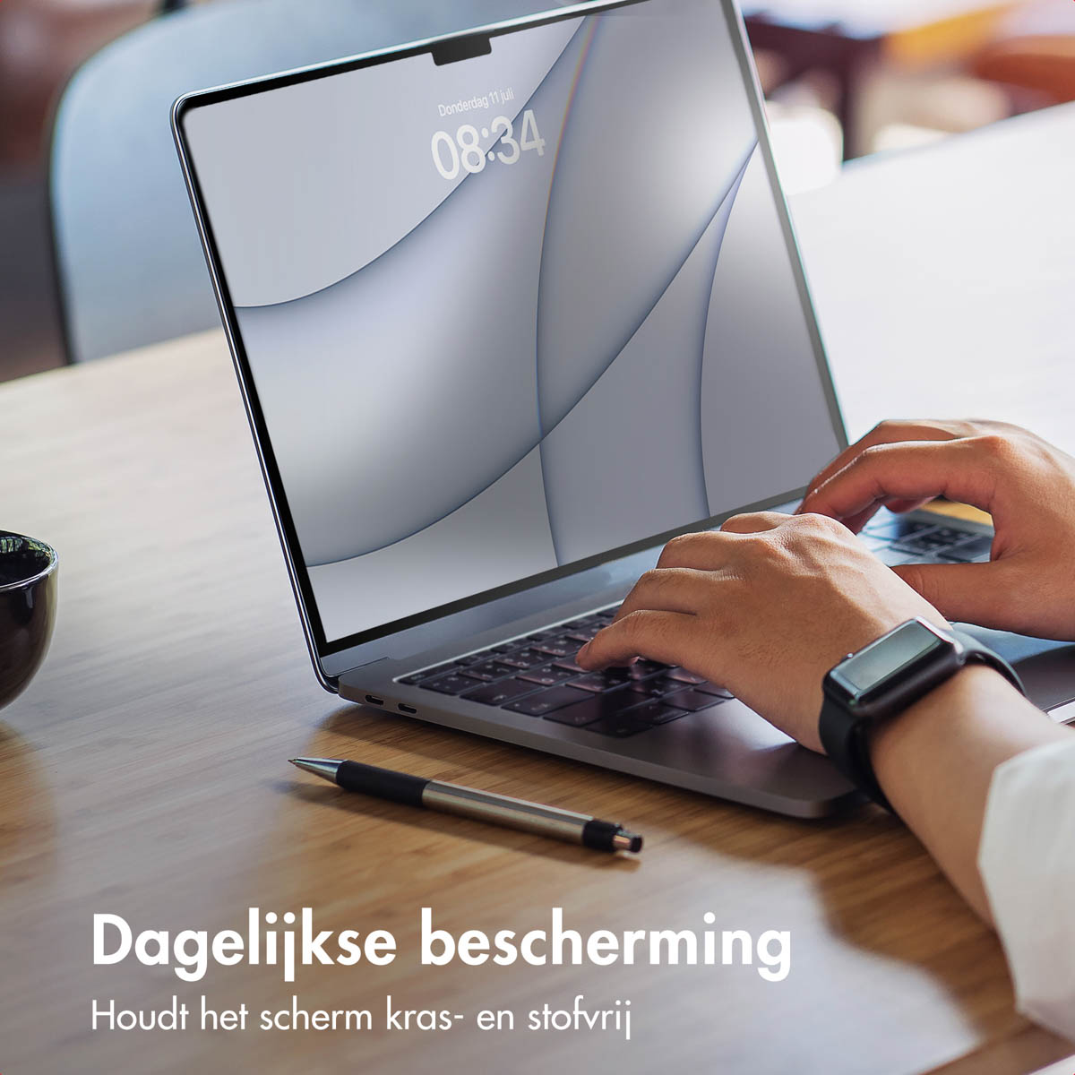 Persoon typt op laptop met schermprotector, pen en kopje op houten tafel.