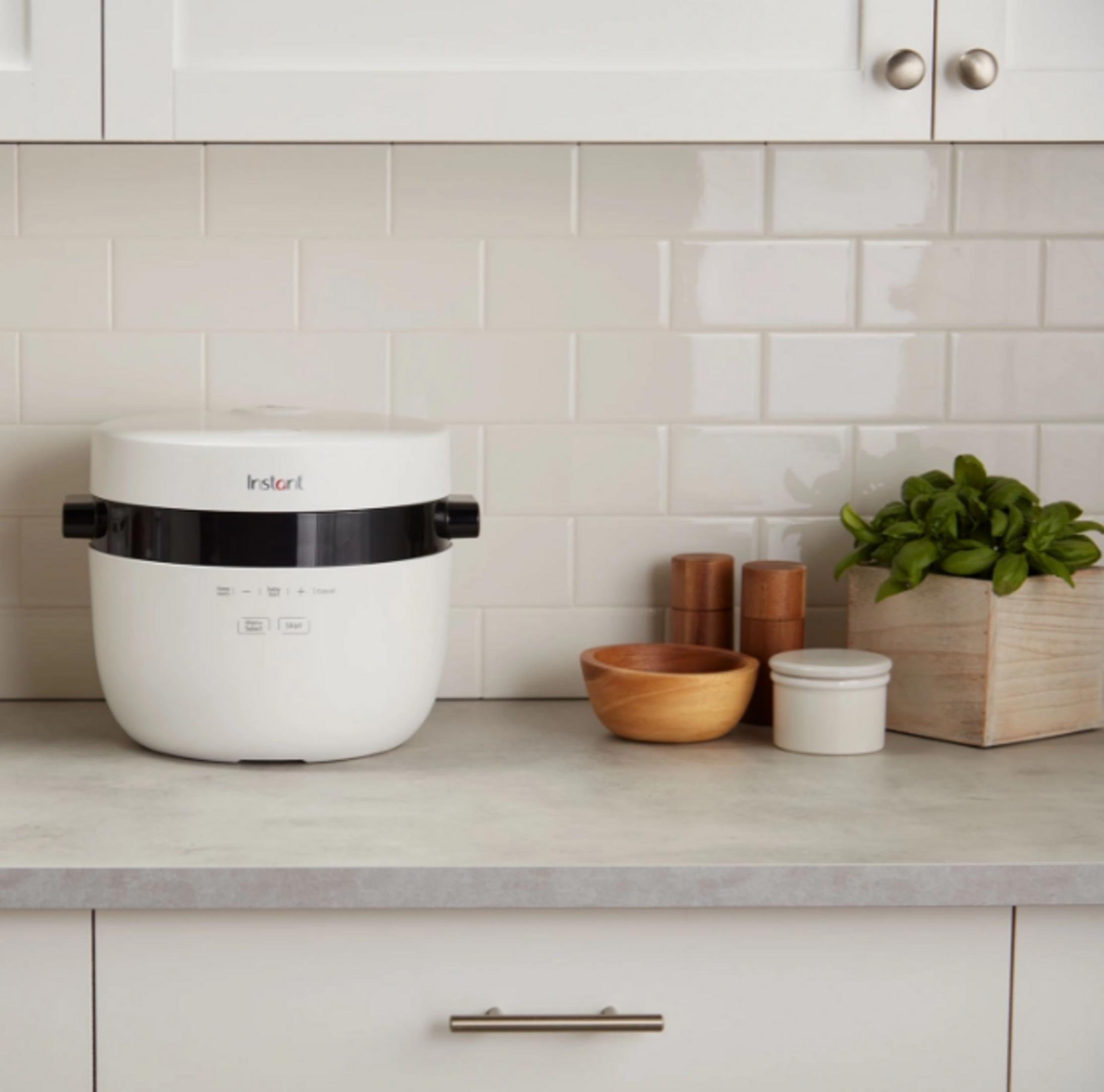 Biały Instant Pot stoi na blacie obok drewnianych miseczek i bazylii.