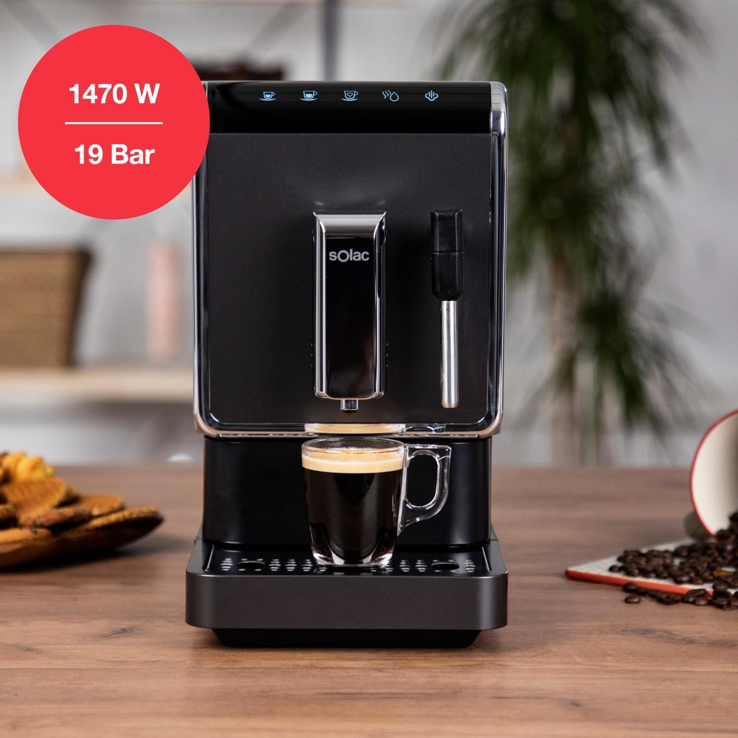 Una cafetera negra con un vaso de espresso, galletas y granos de café.