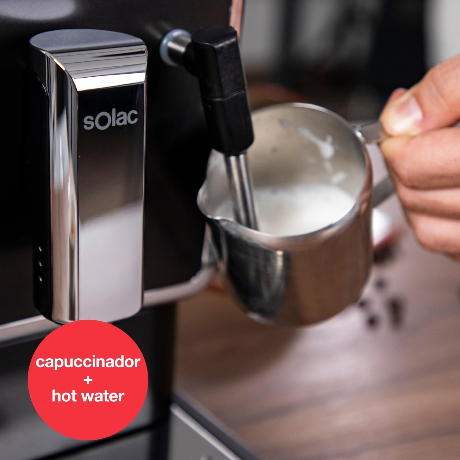 Una mano sostiene una jarra de metal con leche espumosa bajo el vaporizador de una cafetera.