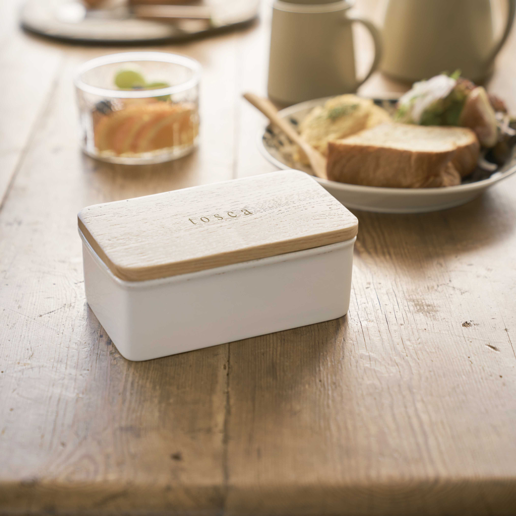 Contenitore bianco con coperchio in legno su tavolo di legno, con cibo vicino.