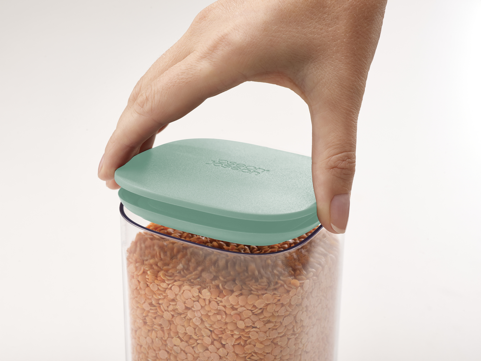 Una mano chiude un contenitore di lenticchie rosse con coperchio verde menta.