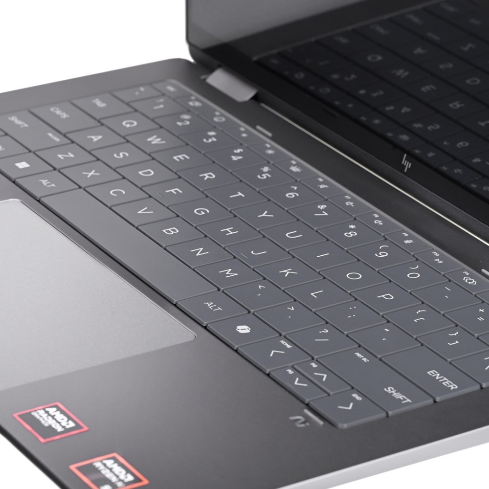 Zbliżenie szarej klawiatury laptopa z touchpadem i naklejkami AMD.