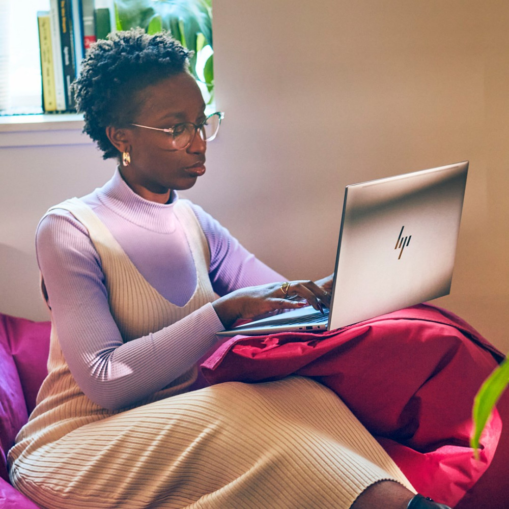 Kobieta w okularach pisze na laptopie, siedząc na czerwonej poduszce.