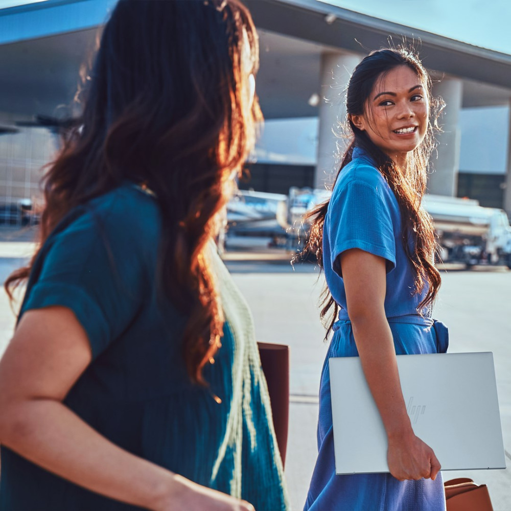 Dwie kobiety idą po płycie lotniska, jedna niesie laptopa.