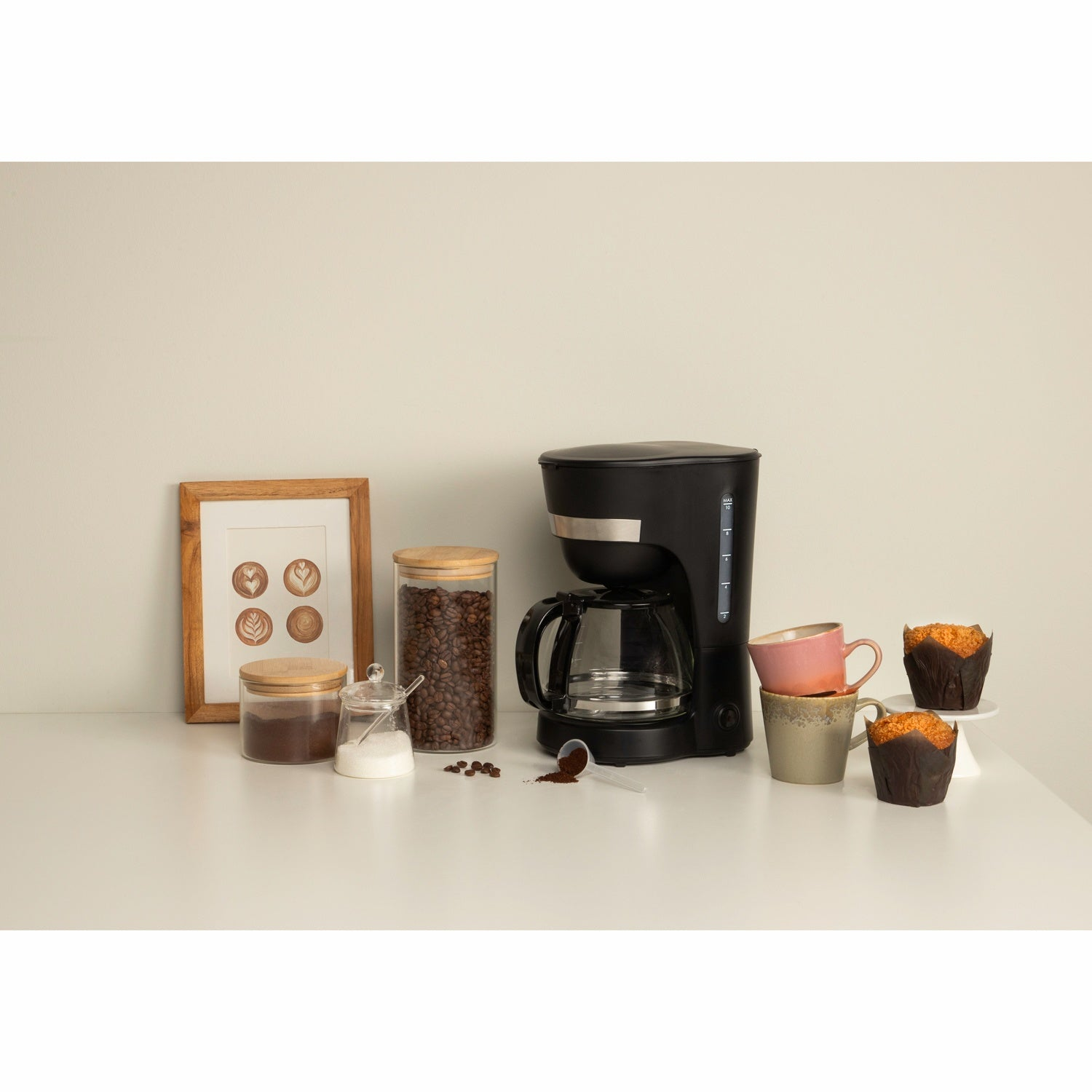 Koffiezetapparaat met bonen, suiker, muffins en kopjes op tafel.